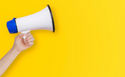 Hand holding megaphone on yellow background.