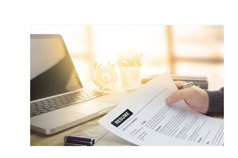 Individual holding a printed resume in front of a laptop.